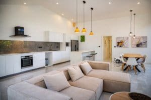 Bright open-plan kitchen and living area with white cabinets, pendant lights, and cozy gray sofa in.