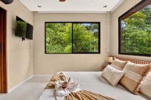 Cozy modern bedroom with large windows overlooking lush trees and a king-size bed.