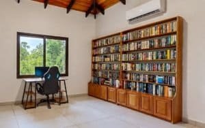 Home office with large bookcase, desk, and chair in tropical room.