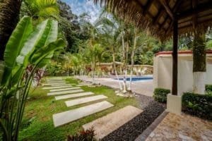 Lush tropical garden with pathway, pool, and shaded seating area in Dominical.