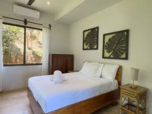 Bright bedroom with white bedding, wooden furniture, and tropical decor.