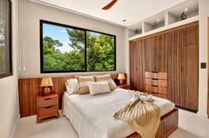 Luxurious tropical bedroom with large window overlooking greenery and wooden built-in wardrobe.