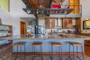 Panoramic sunset ocean view kitchen bar with rustic wood cabinetry and modern appliances.