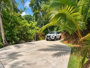 White SUV on a curved concrete driveway surrounded by tropical palm trees and greenery.