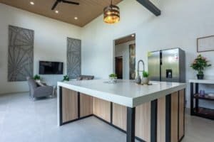 Modern kitchen with island, pendant light, and stainless steel refrigerator in a bright living space.