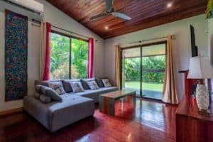 Bright living room with large windows to garden, leather sofa, wooden ceiling and tropical scenery.
