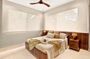 Luxurious bedroom with large windows, wooden headboard, and neutral decor.