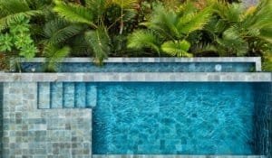Infinity pool with blue water and tropical greenery backdrop.