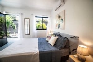 Bedroom with large window, white walls, and tropical outside view.
