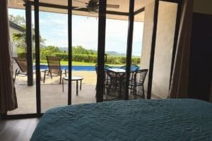 Bedroom with panoramic pool and valley view through glass doors, Costa Rica coast.