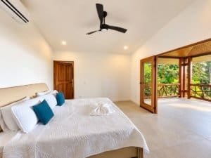 Spacious bedroom with king bed, white bedding, and balcony doors opening to lush Costa Rica scenery.