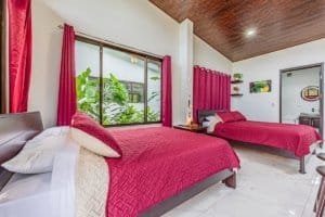 Two red-gewed bedrooms with large window and plants in a bright master suite.