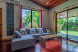 Turn-key coastal home living room with panoramic glass doors to garden and tropical view.