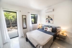 Bedroom with large bed, white walls, tropical decor and sliding door to patio.