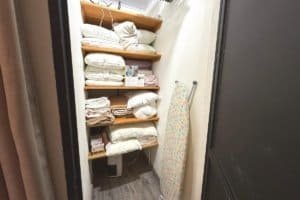 Well-organized linen closet with stacked towels, blankets, and an ironing board in a small utility.