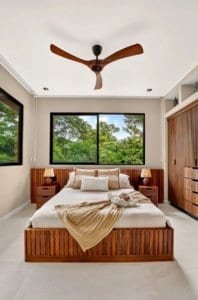 Luxurious bedroom with wooden bed, large windows, ceiling fan and greenery view.