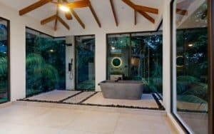 Modern indoor-outdoor bathroom with freestanding tub and glass walls surrounded by lush greenery.