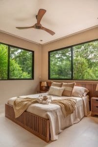 Luxury jungle bedroom with large windows and ceiling fan, overlooking lush Costa Rica greenery.