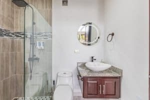 Contemporary bathroom with glass shower, round mirror, and granite vanity.