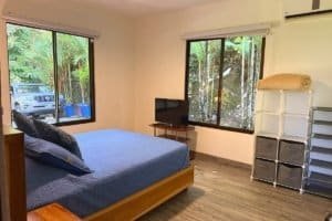 Bedroom with blue bed, large windows, and storage shelves in a tropical home.