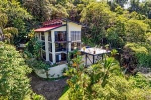Panoramic sunset ocean view villa surrounded by lush rainforest and palm trees.