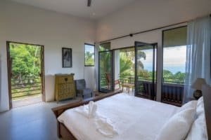Spacious bedroom with ocean view, balcony, and tropical surroundings.