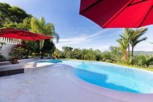 Beautiful pool with mountain view, lush greenery, and red umbrellas in Costa Rica.