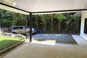 Covered patio with gravel driveway and lush tropical plants in background.