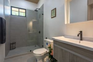 Modern bathroom with glass shower, single vanity, and neutral tones in Dominical real estate.