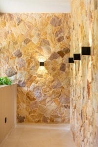 Interior stone wall hallway with warm wall sconces and beige tiled floor.