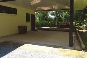 Covered patio area with bench and lush tropical trees in the background.