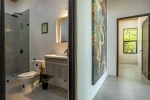 Creekside home bathroom with glass shower, modern vanity, and adjacent hallway.