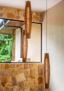Three pendant wooden lights in a modern tropical interior with stone wall and large window.