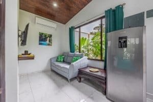 Turnkey Costa Rica living room with gray sofa, tropical plants, and stainless steel fridge.