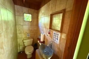 Small bathroom with stone sink, mirror, toilet, and tropical decor in Dominical.