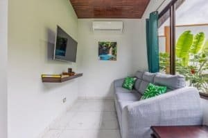Dominical Costa Rica - bright living room with gray sofa, wall-mounted TV, and sliding glass door to.