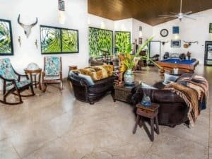 Bright living room with tropical decor, pool table, and large windows showing greenery.