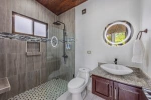 Modern bathroom featuring walk-in shower, circular window, and granite vanity.
