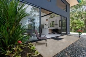 Creekside modern house with glass walls, patio seating, and garden in Costa Rica.