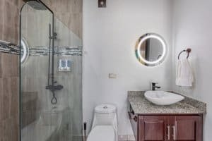 Modern bathroom with glass shower, circular mirror, and granite countertop.