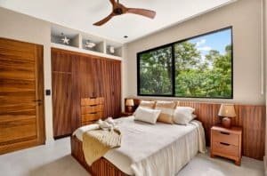 Bedroom with wooden paneling, large window overlooking trees, ceiling fan, neutral tones.