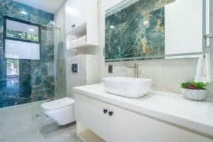 Ocean view bathroom with white vanity, vessel sink, marble countertops, and glass shower.