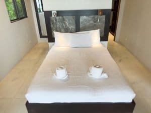 Modern bedroom with ocean view, white bedding, and two cups on the bed.