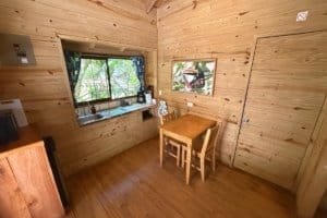 Interior of a wooden jungle hotel room with a small table, chairs, and window view.