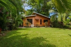 Dominical coastal home with wooden facade, surrounded by lush tropical trees and green lawn.