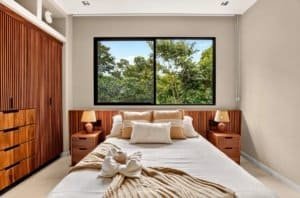 Bedroom with large window overlooking trees and greenery.