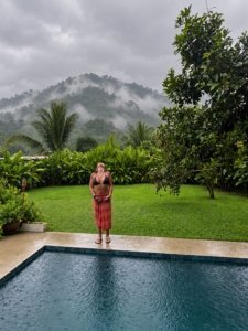 Woman by pool with lush greenery and mountains in the background.
