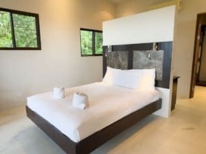 Modern bedroom with ocean view, white bedding, and large windows in Dominical.