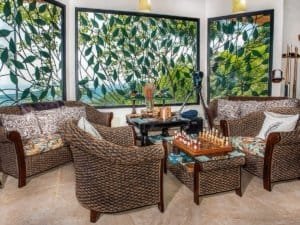 Cozy indoor lounge with wicker furniture and large leafy windows.