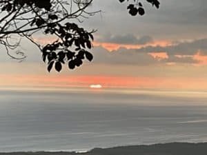 Beautiful ocean sunset view from Dominical with clouds and silhouetted tree branches.